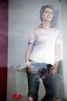 Portrait of smiling woman looking through window - TOYF001195