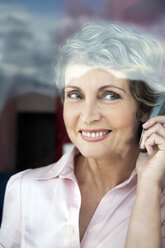 Porträt einer lächelnden Frau, die beim Blick durch das Fenster telefoniert - TOYF001196