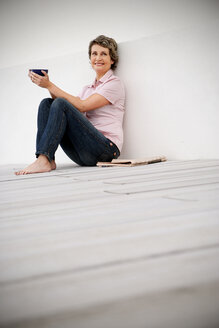 Spain, Mallorca, portrait of smiling woman with newspaper and bowl of coffee - TOYF001199