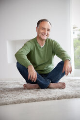 Portrait of smiling man sitting on a carpet at home - TOYF001400