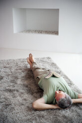 Mature man lying relaxing on a carpet at home - TOYF001203