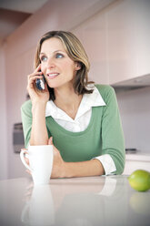 Porträt einer lächelnden Frau beim Telefonieren in der Küche - TOYF001214