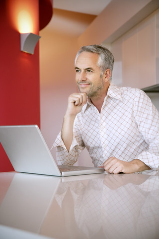 Porträt eines lächelnden Mannes mit Laptop, der in die Ferne schaut, lizenzfreies Stockfoto