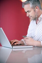 Porträt eines Mannes mit Kopfhörern, der eine Kreditkarte hält und einen Laptop benutzt - TOYF001232
