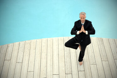 Barefoot businessman wearing black suit standing in front of swimming pool doing yoga exercise - TOYF001227