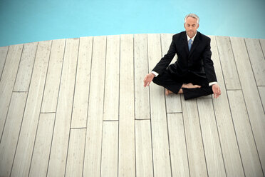 Barefoot businessman wearing black suit meditating in front of swimming pool - TOYF001226