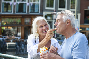 Netherlands, Amsterdam, happy senior couple eating French Fries - FMKF002047