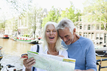 Netherlands, Amsterdam, happy senior couple with map at town canal - FMKF002022