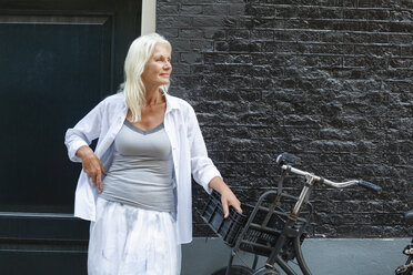 Niederlande, Amsterdam, ältere Frau mit Fahrrad vor einem Haus stehend - FMKF002021