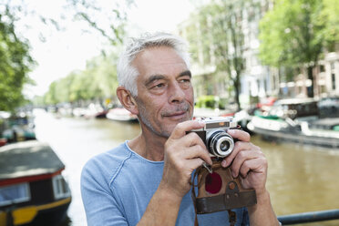 Niederlande, Amsterdam, älterer Mann, der ein Bild mit einer analogen Kamera am Stadtkanal macht - FMKF002016