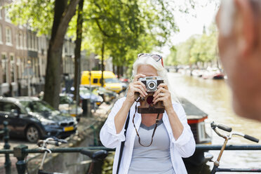 Niederlande, Amsterdam, ältere Frau, die ein Bild mit einer analogen Kamera am Stadtkanal macht - FMKF002015