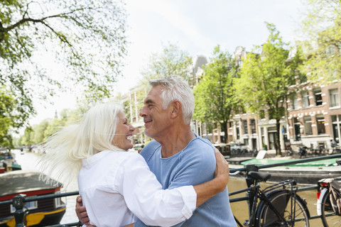 Niederlande, Amsterdam, glückliches älteres Paar, das sich am Stadtkanal umarmt, lizenzfreies Stockfoto
