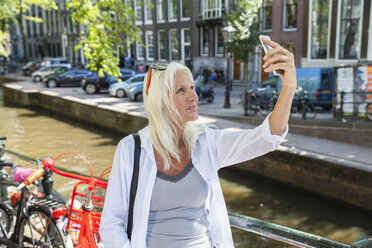 Niederlande, Amsterdam, ältere Frau macht ein Selfie am Stadtkanal - FMKF002008