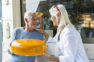 Niederlande, Amsterdam, älteres Ehepaar sitzt auf einer Bank und hält einen Laib Käse - FMKF002003