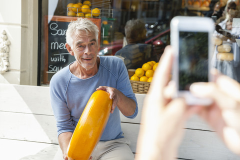 Netherlands, Amsterdam, cell phone picture of senior man sitting on bench holding loaf of cheese stock photo