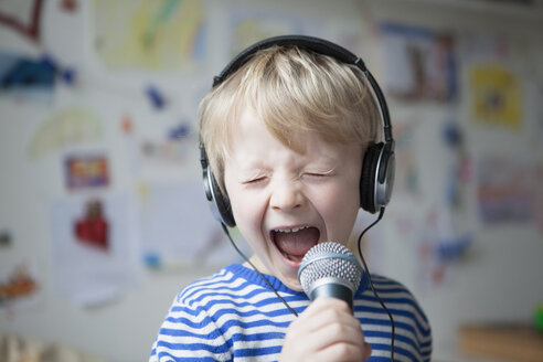 Porträt eines singenden kleinen Jungen mit Kopfhörern und Mikrofon - RBF002990