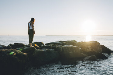 France, Pornichet, woman standing on rocks at seafront by sunset - GEMF000322