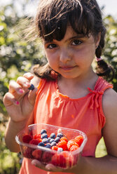 Porträt eines kleinen Mädchens mit einer Plastikschachtel mit Himbeeren und Heidelbeeren - MGOF000577
