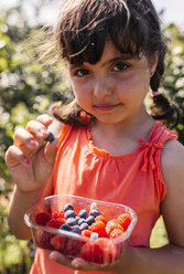 Portrait of little girl with plastic box of raspberries and blueberries - MGOF000577