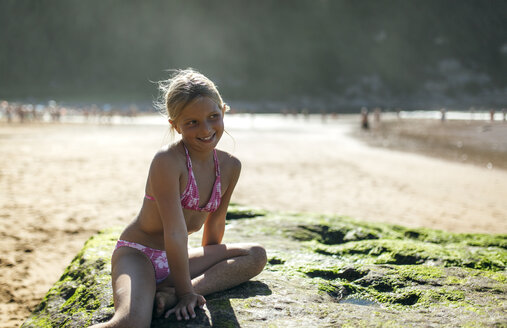 Porträt eines blonden kleinen Mädchens, das auf einem Felsen am Strand sitzt - MGOF000588