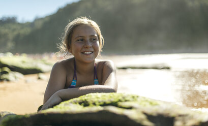 Porträt eines lächelnden Mädchens, das sich an einen Felsen am Strand lehnt - MGOF000600