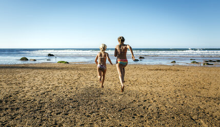 Rückenansicht von zwei Schwestern beim Laufen am Strand - MGOF000608