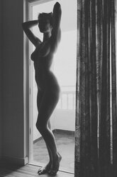 Nude woman standing in balcony door frame - MFF002094