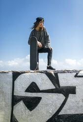 Porträt eines jungen Skateboarders mit Baseballmütze, der an einer Wand steht - MGOF000616