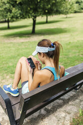 Junge Frau in Sportkleidung mit Smartphone, auf einer Bank sitzend - MGOF000639