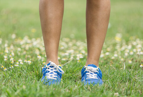 Füße einer Frau in Turnschuhen auf Gras stehend - MGOF000644