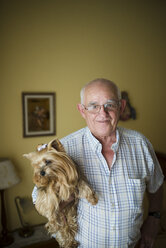 Porträt eines lächelnden älteren Mannes, der seinen Yorkshire Terrier hält - RAEF000454