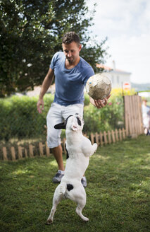 Mann mit einem Ball, der mit einer französischen Bulldogge spielt - RAEF000430