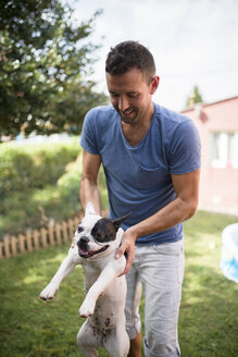 Mann mit französischer Bulldogge in einem Garten - RAEF000431