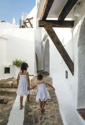 Spanien, Balearische Inseln, Menorca, Binibeca, Rückenansicht von zwei kleinen Schwestern, die Hand in Hand gehen, lizenzfreies Stockfoto