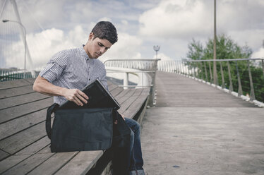 Spain, Ferrol, young man taking his laptop out of a bag - RAEF000484