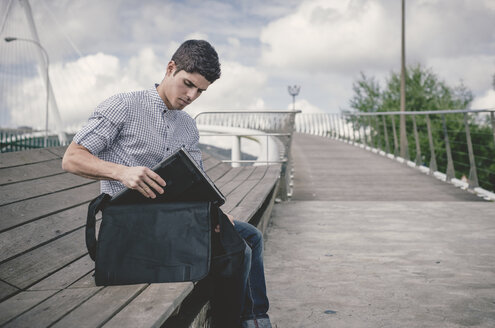 Spanien, Ferrol, junger Mann holt seinen Laptop aus einer Tasche - RAEF000484