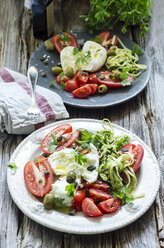 Zwei Teller mit Büffelmozzarella, Tomaten, Zucchinischeiben, Kapern, grünen Oliven und Gewürzen - ODF001278