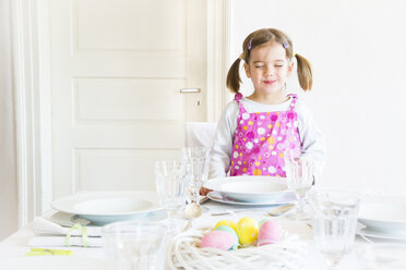 Porträt eines lächelnden kleinen Mädchens mit geschlossenen Augen, das hinter einem gedeckten Tisch steht - LVF003777