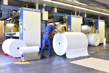 Mann bewegt Papierrolle in einer Druckerei - LYF000470