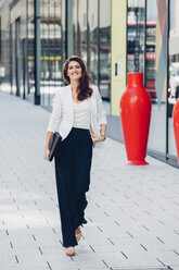 Smiling businesswoman walking on pavement - CHAF001401