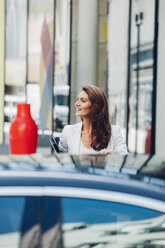 Smiling businesswoman outdoors behind car - CHAF001406