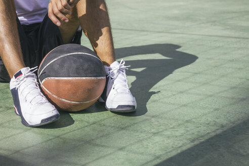 Mann auf dem Boden sitzend mit Basketball zwischen seinen Füßen - ABZF000116