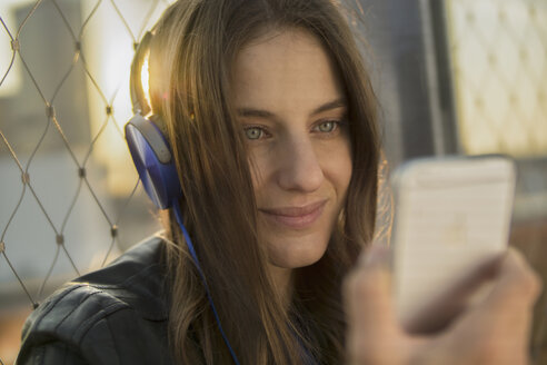 Deutschland, Frankfurt, Porträt einer lächelnden Frau, die mit Kopfhörern Musik hört und auf ihr Smartphone schaut - RIBF000257