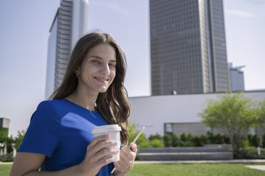 Germany, Frankfurt, portrait of smiling woman with coffee to go and mini tablet - RIBF000275