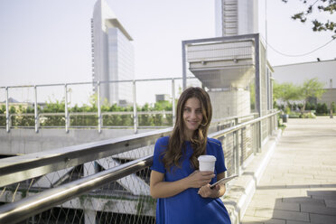 Germany, Frankfurt, portrait of smiling woman with coffee to go and mini tablet - RIBF000276