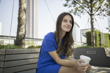 Germany, Frankfurt, portrait of smiling businesswoman sitting on a bench with coffee to go - RIBF000277