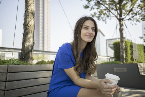 Deutschland, Frankfurt, Porträt einer lächelnden Geschäftsfrau auf einer Bank sitzend mit einem Kaffee zum Mitnehmen - RIBF000277