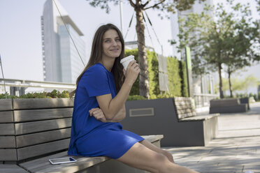 Deutschland, Frankfurt, Geschäftsfrau auf einer Bank sitzend mit Kaffee zum Mitnehmen - RIBF000278