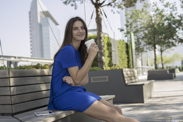 Germany, Frankfurt, businesswoman sitting on a bench with coffee to go - RIBF000278