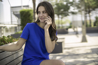 Lächelnde Geschäftsfrau, die auf einer Bank sitzt und mit einem Smartphone telefoniert - RIBF000281